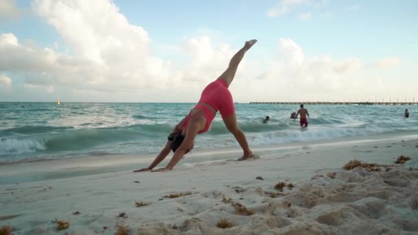 Disparo de cámara constante. Mujer joven practicando yoga en la playa cerca del mar. — Vídeos de Stock