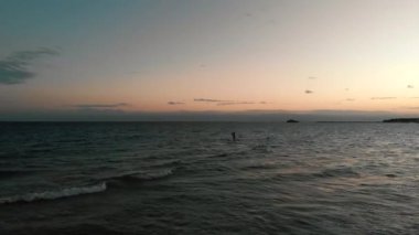 Günbatımında okyanusta sörf tahtası çalışırken çekilmiş bir fotoğraf.