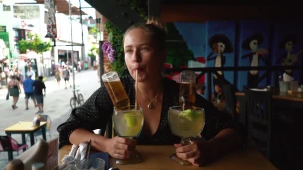 Красивая молодая женщина улыбается, наслаждаясь алкогольными коктейлями возле барной стойки. — стоковое видео