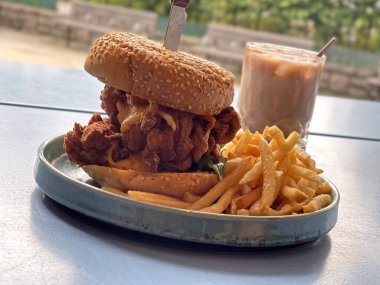 The crispy chicken, sesame bread cheese burger with French fries on dish and ice coffee