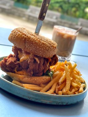 The vertical crispy chicken, sesame bread cheese burger with French fries on dish and ice coffee