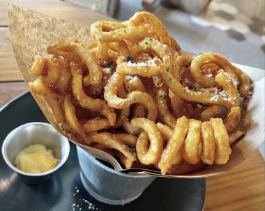 The horizontal crispy curly French fries inside silver bucket with sauce at cafe