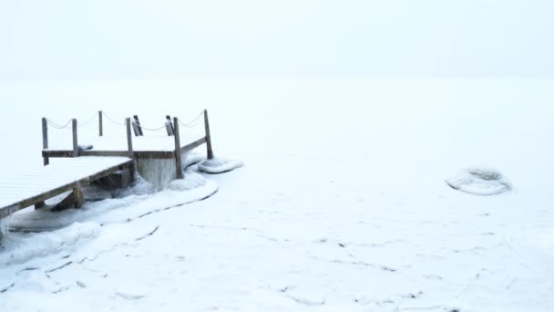 どこでも白い雪だけです 反対側の海岸は雪がたくさん降るときには見えにくいです 唯一の桟橋は白い風景の中に立っている — ストック動画