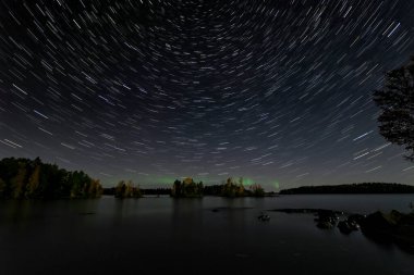 Gölün arkasında yıldız yolları ve kuzey ışıkları parlıyor. Kısa çizgiler..