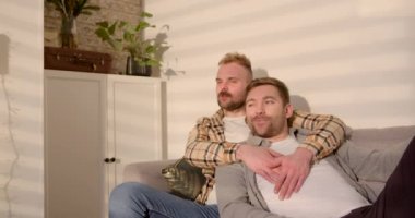 Bir LGBTQI 'nin ön görüntüsü. Aynı cinsiyetten erkek çift oturma odalarında oturmuş kanepede dinleniyor, konuşuyorlar ve televizyon izliyorlar..
