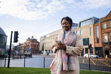 Kasaba merkezinde gülümseyen ve cep telefonu kullanan bir kadın.