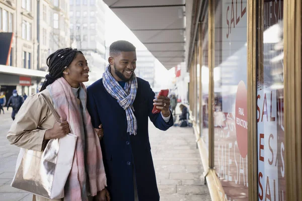 Vrolijk Paar Etalages Winkelen Het Controleren Van Mobiele Telefoon Glimlachen — Stockfoto