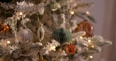 A close-up slowly panning shot of a Christmas tree decorated with golden-orange shiny balls and lights.