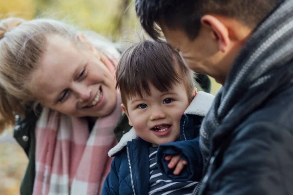 A family spending a day in nature together in Northumberland, North East England during Autumn. The parents are looking at their baby boy while the boy looks at the camera and smiles.