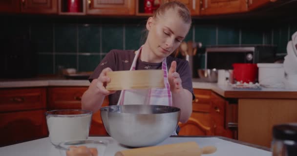 Žena tahá mouku přes síto v kuchyni a peče croissanty. — Stock video