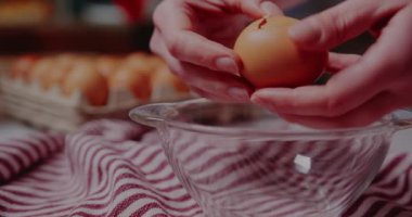Female hand breaks fresh chicken egg into bowl.