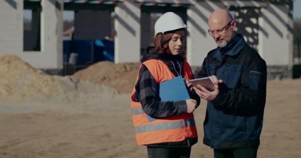 Ingenieros concentrados discutiendo, examinando y desarrollando en el sitio de construcción — Vídeos de Stock