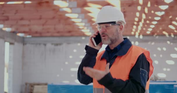 Undervisning Arbetstagaren talar i mobilen på byggarbetsplatsen — Stockvideo