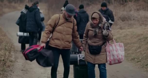 Hombre maduro ayudando a la mujer refugiada que lucha con tirar del equipaje. — Vídeo de stock