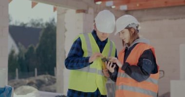 Genç iş arkadaşları inşaat alanında akıllı telefondan tartışıyorlar.