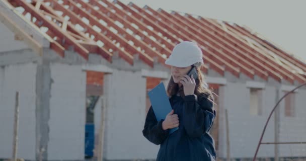 Female civil engineer talking on smartphone at construction site — стоковое видео