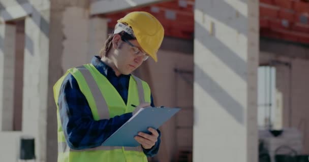 Young male construction worker writing on clipboard — Video
