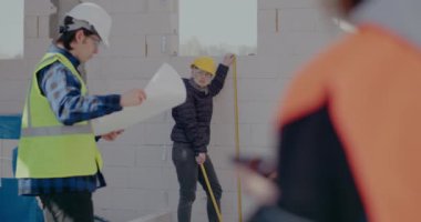 Kadın müteahhit duvarları ölçüyor. İşçilerle tartışıyor.