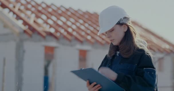 Young female architect writing on clipboard at incomplete site — Vídeo de Stock