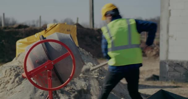 Мужчина строитель кладет цемент в смеситель с лопатой — стоковое видео