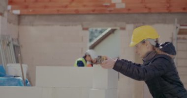 Kadın müteahhit beton duvarı düzeyi ile inceliyor.