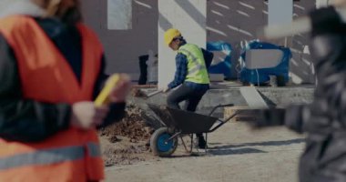 Erkek işçi olay yerinde el arabasıyla kum topluyor.