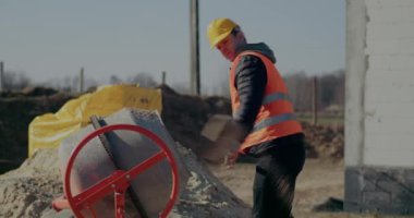 Erkek işçi çimentoyu kürekle karıştırıyor.