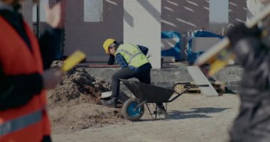 Erkek işçi el arabasında kürekle kum topluyor.
