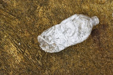 Kahverengi beton zeminde şeffaf plastik şişenin buruşuk hali, çözülmesi zor çöpler.