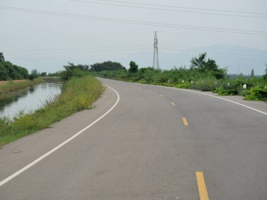 Sulama ve ulaşım sistemi, Tayland 'da dağ ve yüksek voltaj kulesi olan kanal boyunca açık eğimli asfalt yol.