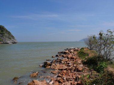 Rocky reef and stone in the green water of sea with mountain and island in background, Beach with blue sky and white cloud at Khao Sam Roi Yot National Park, Thailand