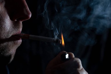 Sigara içen genç bir adamın portresi. Yakışıklı genç adam düşünceli ve sakince sigara içiyor. Erkek güzelliği, moda.