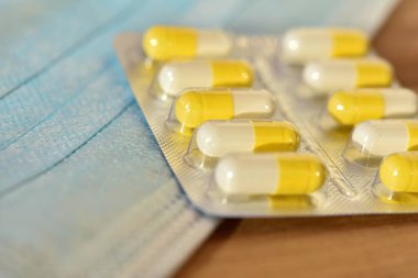 Tıbbi bir maskenin arka planında kapsüllerdeki beyaz-sarı haplar. bulanık