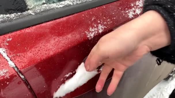 Een vrouwenhand verwijdert sneeuw uit de deurkruk van de auto — Stockvideo