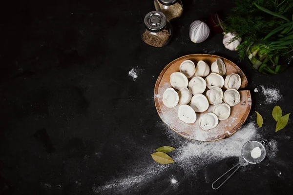 Geleneksel Rus hamur köfteleri kesim tahtasında, mantı, pelmeni, koyu arka plan; üst görünüm