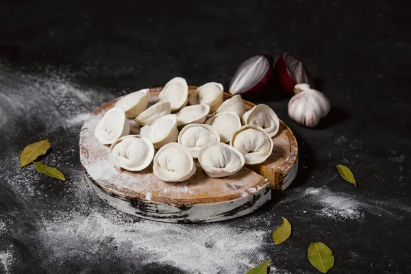 Geleneksel Rus hamur köfteleri kesim tahtasında, ravioli, pelmeni, koyu arka plan