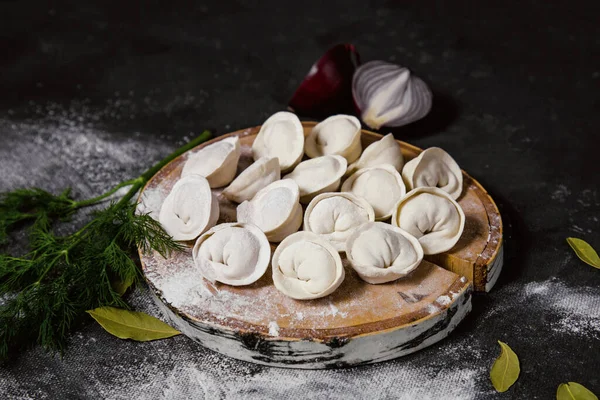 Geleneksel Rus hamur köfteleri kesim tahtasında, ravioli, pelmeni, koyu arka plan