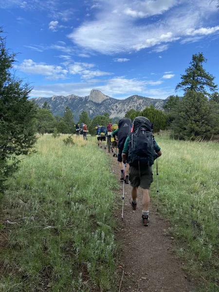 Arka planda Zaman Dişi olan karışık ağaçların arasında yürüyüş yapan bir grup. 2022 Yaz sezonunda Philmont Scout Çiftliğinde çekildi.