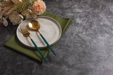 Beton zeminde gri tabağı ve altın çatal bıçak takımı olan son moda sofra takımı. Metin için boşluk kopyala, üst görünüm. Sonbahar çiçekleriyle İskandinav tarzı şablon