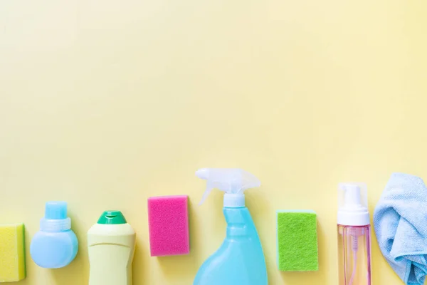 Cleaning concept - cleaning supplies on pastel yellow background, top view