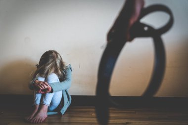child abuse, violence concept - young girl scared sitting on the floor, parent holds belt, physical punishment. Toned