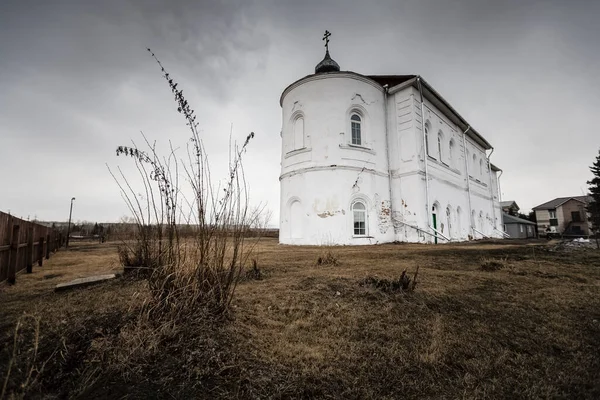 Gri gökyüzünün altındaki ortodoks kilisesinde ön planda kuru çimenler var.