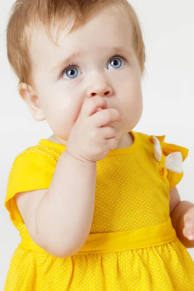 Sarı elbiseli küçük kız parmağını ısırıyor.