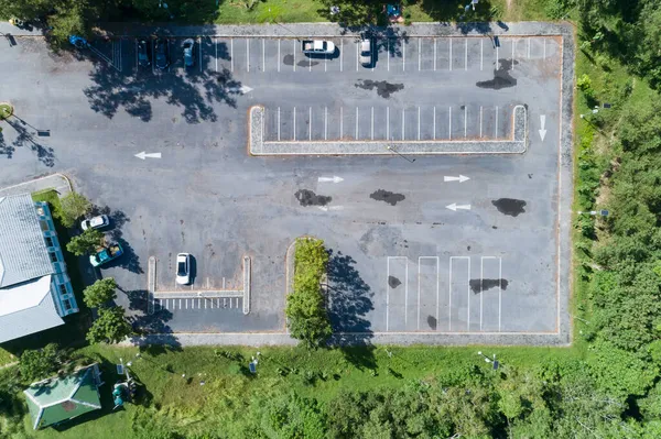 Beton araba parkında park etmiş, caddede beyaz çizgi halinde trafik işaretleri olan bir arabanın hava manzarası. Araba manzarasının üstünde park yerinde sıra halinde araba park alanının dışında..