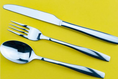 Çatal, bıçak ve kaşık seti sarı kağıtta izole edilmiş..