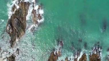 Deniz kıyısındaki kayaların tepesindeki hava aracı kamerası kayalara çarpan inanılmaz deniz dalgaları.