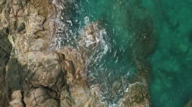 Deniz kıyısındaki kayalara çarpan dalgaların havadan görünüşü. Üstten aşağı ve denize doğru eğiliyor. Muhteşem Rocky sahili.