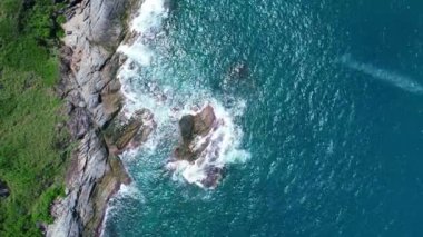Mavi bir okyanusta deniz kıyısındaki kayaların tepesindeki insansız hava aracı kamerası. Güzel deniz yüzeyi. Kayalara çarpan inanılmaz deniz dalgaları.