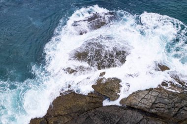 Aerial view Drone camera top down of seashore rocks in a blue ocean Turquoise sea surface Amazing sea waves crashing on rocks seascape. High quality image of sea waves in Phuket Thailand