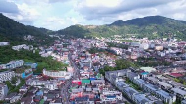 Patong şehrinin insansız hava aracı görüntüsü, Tayland Phuket Adası, farklı yükseklikteki evler. Adanın yeşil tepeleri ve yolda birçok araba var.